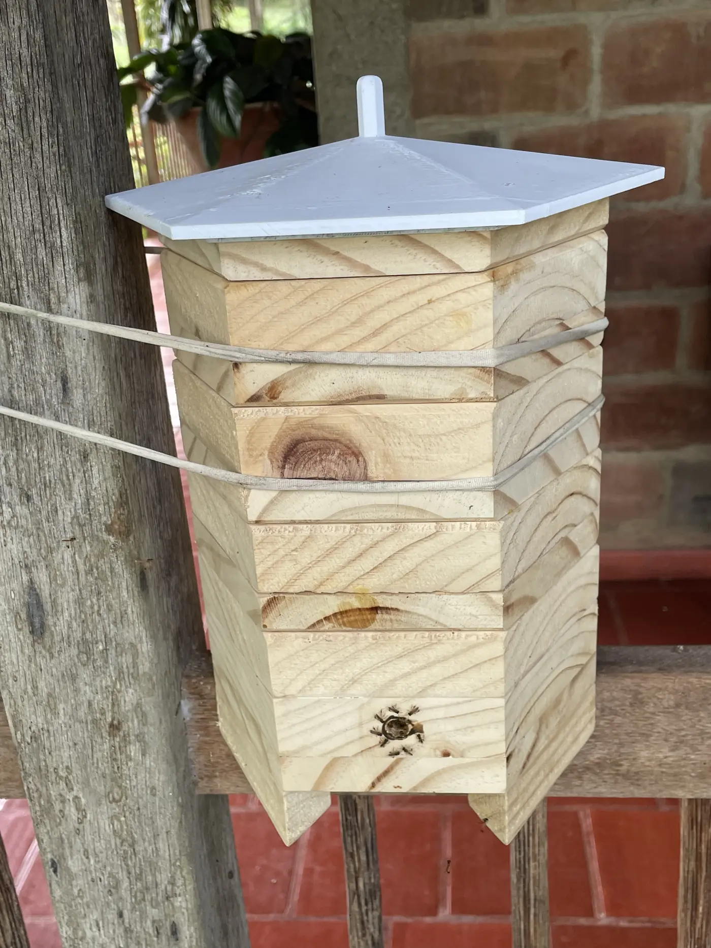 Refugio hexagonal de madera para abejas meliponini, con módulos apilados y techo blanco, sujeto a un poste